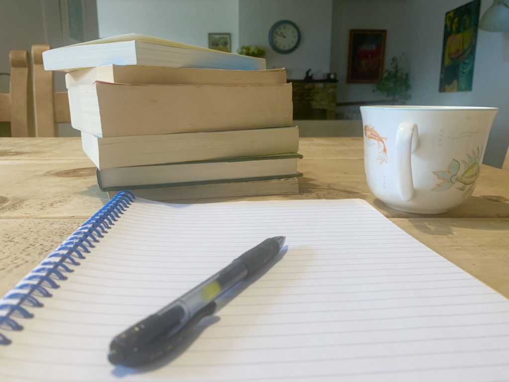 Pile of books with coffee cup, writing pad and pen